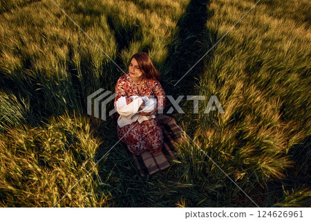 Sitting on the ground. Gorgeous woman is on the agricultural field with her newborn baby 124626961