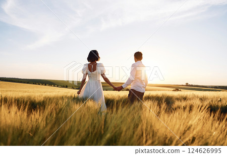 Walking and holding each other by the hands. Couple just married. Together on the majestic agricultural field at sunny day 124626995