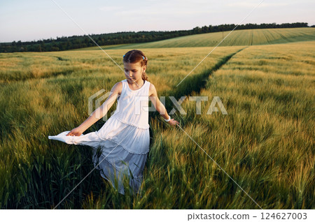Standing and enjoying the walk. Little girl in white clothes is on the agricultural field at sunny day 124627003