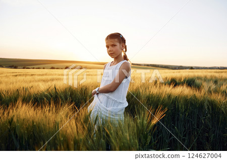 Standing and enjoying the walk. Little girl in white clothes is on the agricultural field at sunny day 124627004