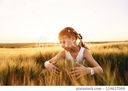Touching the wheat. Little girl in white clothes is on the agricultural field at sunny day Touching the wheat. Little girl in white clothes is on the agricultural field at sunny day 124627009