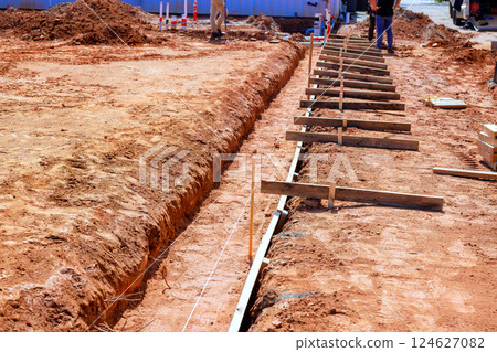 Workers prepare construction site by digging trenches placing wooden supports for foundation framework. Workers prepare construction site by digging trenches placing wooden supports for foundation framework. 124627082