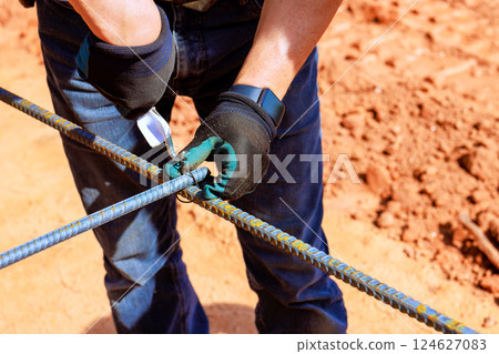 Worker ties steel rebar together at construction site during work day, showcasing skilled craftsmanship Worker ties steel rebar together at construction site during work day, showcasing skilled craftsmanship 124627083
