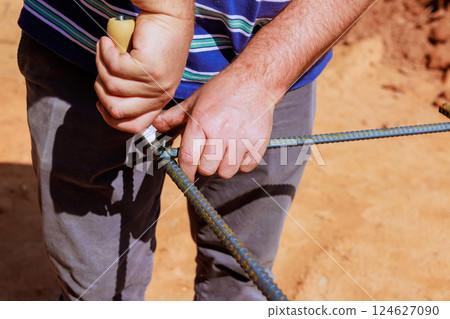 Construction worker carefully secures steel rebar with knot in busy outdoor setting during work day. 124627090