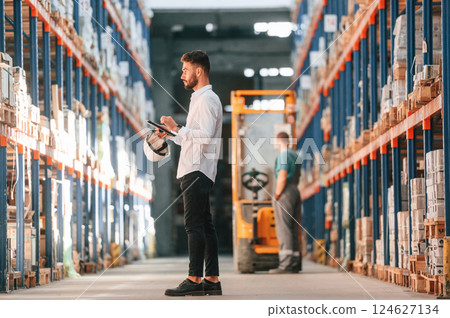 With tablet in hands. Storage worker is in the warehouse with bunch of products 124627134