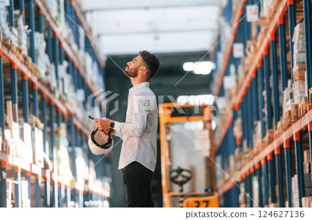 With tablet in hands. Storage worker is in the warehouse with bunch of products With tablet in hands. Storage worker is in the warehouse with bunch of products 124627136