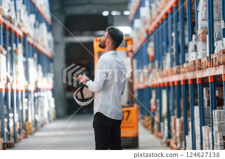 With tablet in hands. Storage worker is in the warehouse with bunch of products With tablet in hands. Storage worker is in the warehouse with bunch of products 124627138