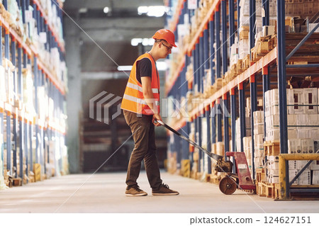 Side view of warehouse worker that is in uniform and hard hat working with cargo Side view of warehouse worker that is in uniform and hard hat working with cargo 124627151