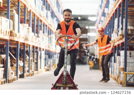 Man riding trolley platform. Having fun. Two storage workers is in the warehouse 124627156