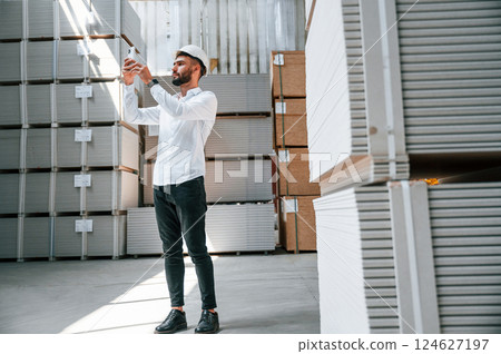 Using phone. Storage worker is in the warehouse with bunch of products 124627197