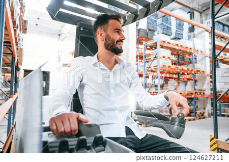 Using cargo moving machine. Storage worker is in the warehouse with bunch of products Using cargo moving machine. Storage worker is in the warehouse with bunch of products 124627211