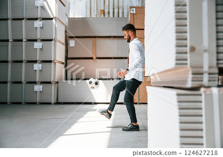 Taking a break, playing with soccer ball. Storage worker is in the warehouse with bunch of products Taking a break, playing with soccer ball. Storage worker is in the warehouse with bunch of products 124627218