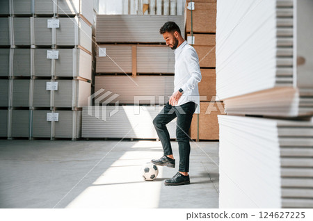 Taking a break, playing with soccer ball. Storage worker is in the warehouse with bunch of products Taking a break, playing with soccer ball. Storage worker is in the warehouse with bunch of products 124627225