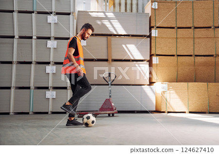 Kicking a soccer ball on the break time. Storage worker is in the warehouse with bunch of products Kicking a soccer ball on the break time. Storage worker is in the warehouse with bunch of products 124627410