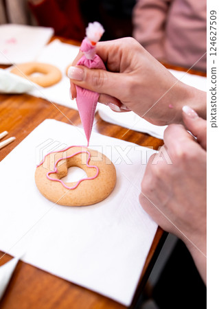 Person icing heart shaped cookie with pink frosting on wooden table 124627509