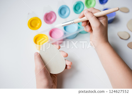 Child painting Easter wooden egg with bright colors and brush for creative art project Child painting Easter wooden egg with bright colors and brush for creative art project 124627552