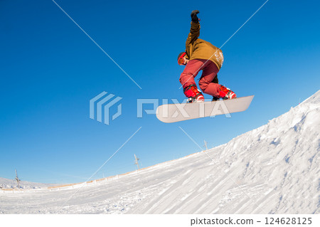 Snowboarder jumping against blue sky Snowboarder jumping against blue sky 124628125