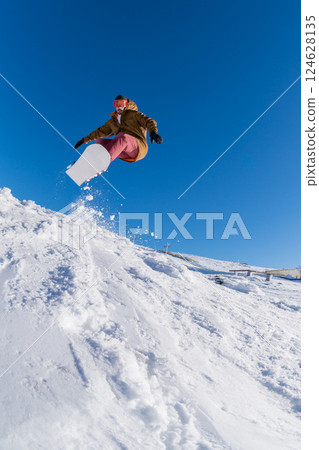 Snowboarder jumping against blue sky 124628135
