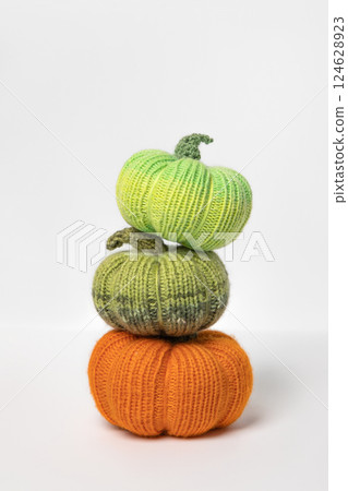Knitted orange and green pumpkins on gray background, front view. Halloween concept. Handmade knitted toys for children and holiday home decor. 124628923