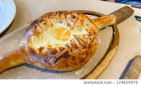 Traditional Georgian khachapuri with melted cheese and egg in the center, served hot on a wooden board 124629978