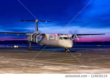 White passenger turboprop airliner taxiing through an airport at dawn 124630114