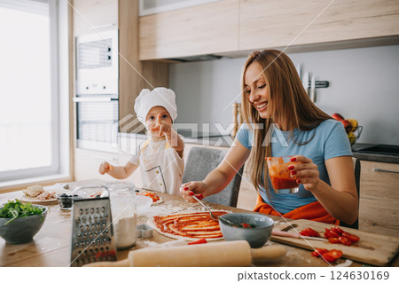 Daughter and mother making pizza together for dinner at the kitchen 124630169