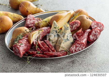 Blue cheese, dry-cured sausages, thyme and pears on a stone table. Blue cheese, dry-cured sausages, thyme and pears on a stone table. 124630507