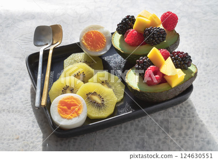 A colorful healthy food with redberry, blackberry and mango on avocado with golden kiwi and boiled egg on vibrant eating ceramic dish. 124630551