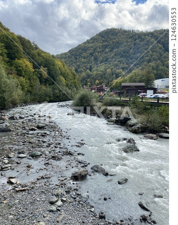 Mountain river Mzymta flowing through a green hills valley in Rosa Khutor, Russia. 124630553