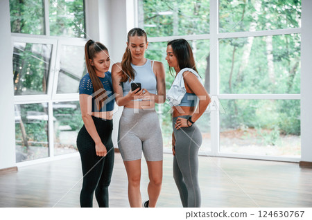 Standing and looking at phone. Group of women practicing fitness in the gym 124630767
