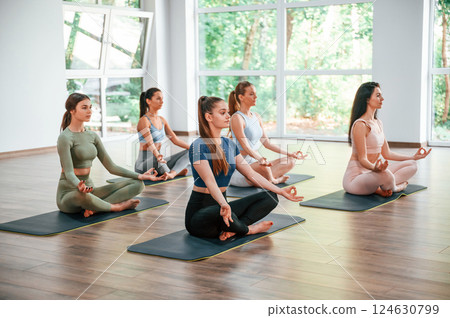 Sitting in lotus pose. Group of women practicing fitness in the gym Sitting in lotus pose. Group of women practicing fitness in the gym 124630799