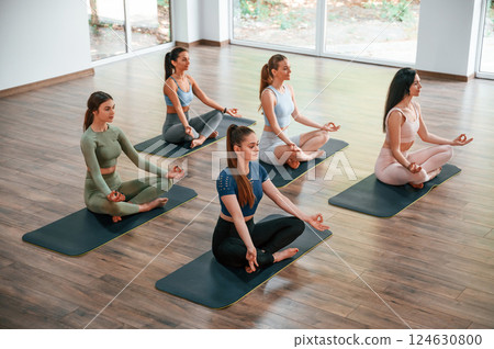 Sitting in lotus pose. Group of women practicing fitness in the gym Sitting in lotus pose. Group of women practicing fitness in the gym 124630800