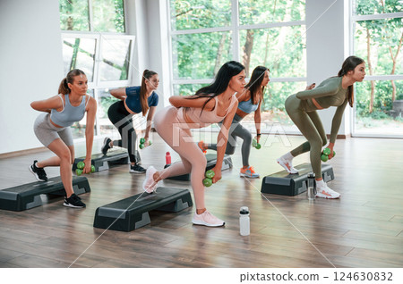 Standing on special platforms and doing legs exercises. Group of women practicing fitness in the gym 124630832