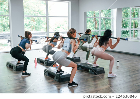 With stick behind the back in hands. Group of women practicing fitness in the gym With stick behind the back in hands. Group of women practicing fitness in the gym 124630840