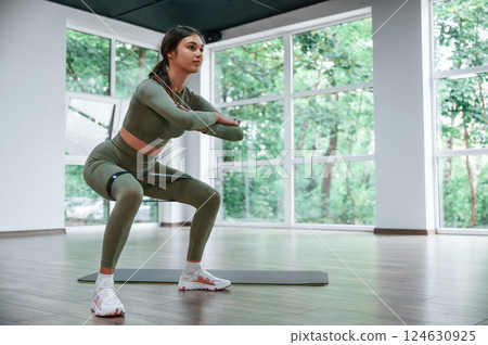 Doing squats. Woman in sportive clothes is having fitness day in the gym Doing squats. Woman in sportive clothes is having fitness day in the gym 124630925