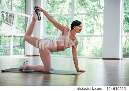 Holding left leg by right hand. Woman in sportive clothes is having fitness day in the gym 124630933