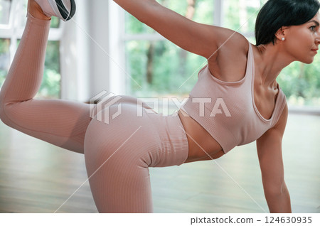Holding left leg by right hand. Woman in sportive clothes is having fitness day in the gym 124630935