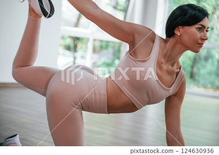 Holding left leg by right hand. Woman in sportive clothes is having fitness day in the gym 124630936