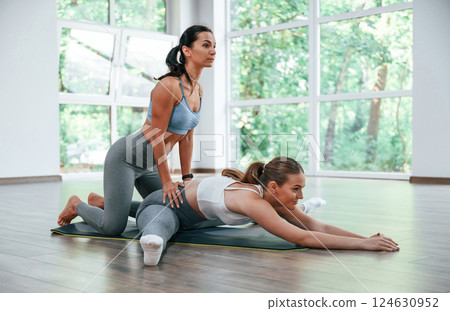 Stretching the legs. Female trainer helping woman with exercises in the gym Stretching the legs. Female trainer helping woman with exercises in the gym 124630952