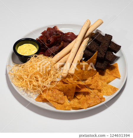 Assorted Snack Platter with Nachos, Breadsticks, Jerky, Cheese Straws and Mustard Dip on White Table 124631394