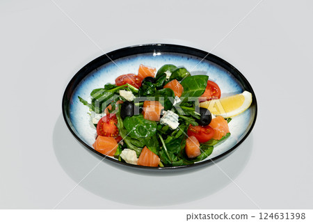 Fresh Salad with Salmon, Spinach, Tomatoes, Olives, Lemon and Cheese Served on Ceramic Plate 124631398