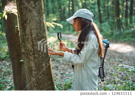 With magnifying glass. Girl is in the forest at summer day time discovering new places With magnifying glass. Girl is in the forest at summer day time discovering new places 124631511