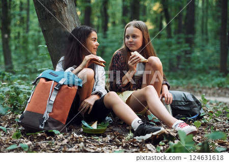 Eating by using plastic forks and plates. Two girls is in the forest having a leisure activity, discovering new places Eating by using plastic forks and plates. Two girls is in the forest having a leisure activity, discovering new places 124631618