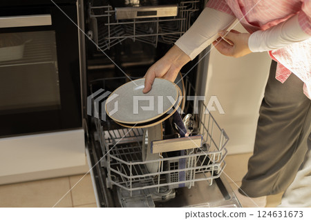 female hands in the frame are putting plates into the dishwasher 124631673