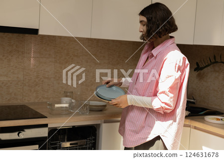 A young woman is putting plates in a kitchen cabinet 124631678