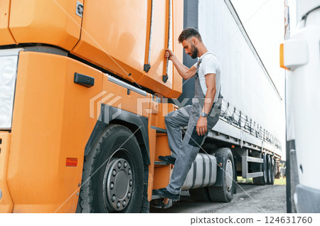Climbing to the vehicle by holding the door. Man in unifrom doing service for big truck vehicle Climbing to the vehicle by holding the door. Man in unifrom doing service for big truck vehicle 124631760