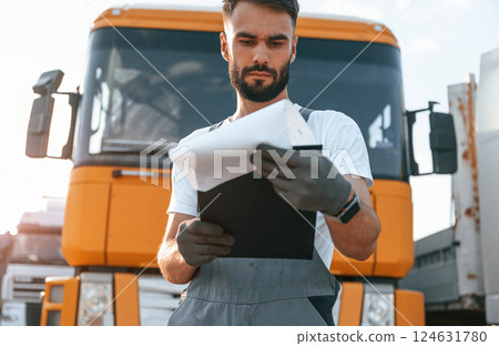 Holding notepad. Quality control. Man in unifrom doing service for big truck vehicle 124631780