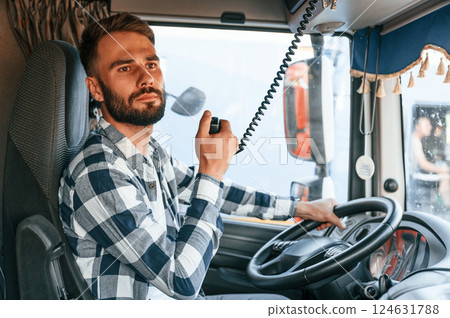 Using radio. Young truck driver is with his vehicle at daytime Using radio. Young truck driver is with his vehicle at daytime 124631788