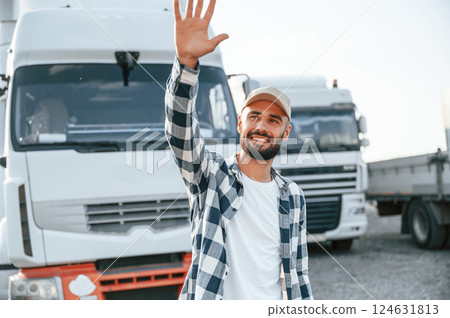 Showing hello gesture by hands and smiling. Young truck driver is with his vehicle at daytime 124631813