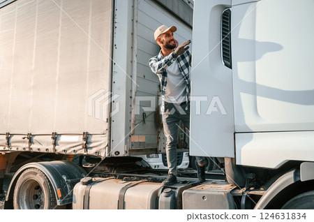 Standing behind the cabin. Young truck driver is with his vehicle at daytime 124631834